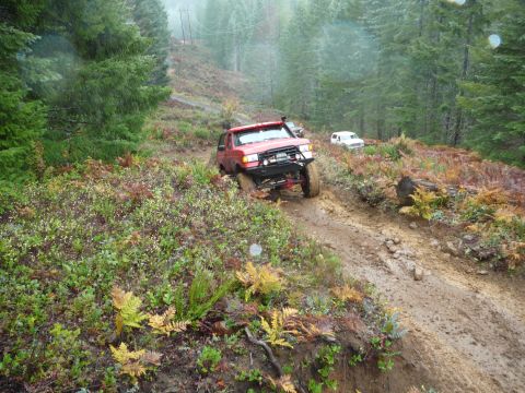 1991 Ford Bronco - Red 1991 Ford Bronco tackles a challenging muddy incline on an off-road trail, with a second vehicle following.
