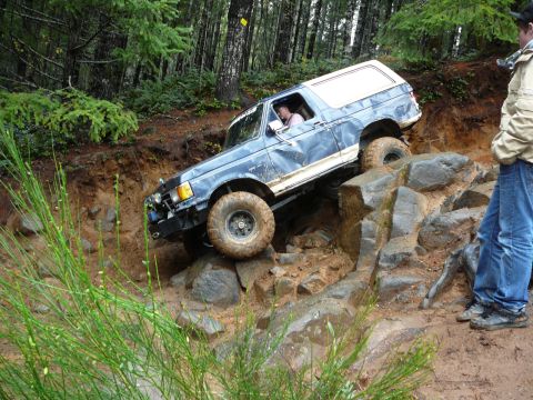 1991 Ford Bronco - A blue Ford Bronco navigates a difficult rocky obstacle on an off-road trail.