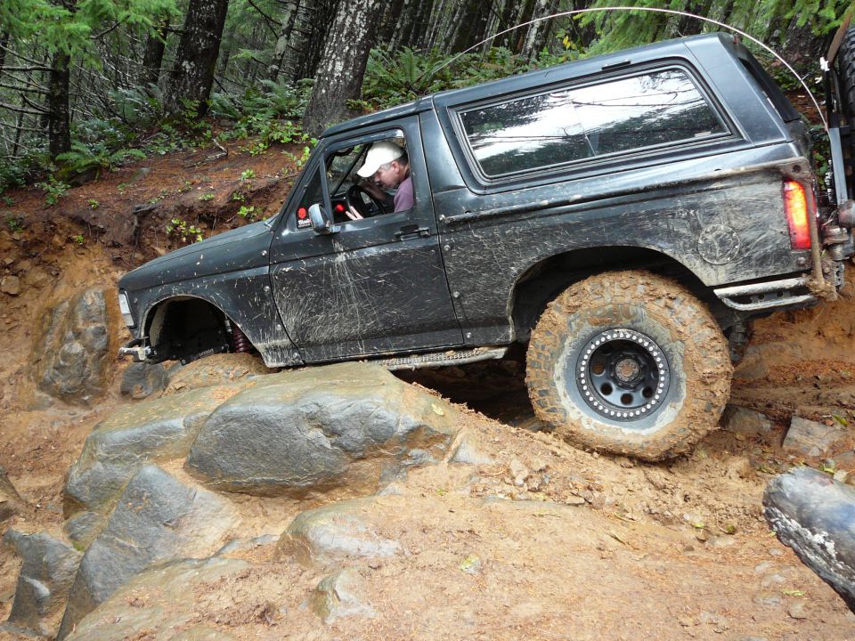 Black 1991 Ford Bronco climbing over rocks on a muddy trail