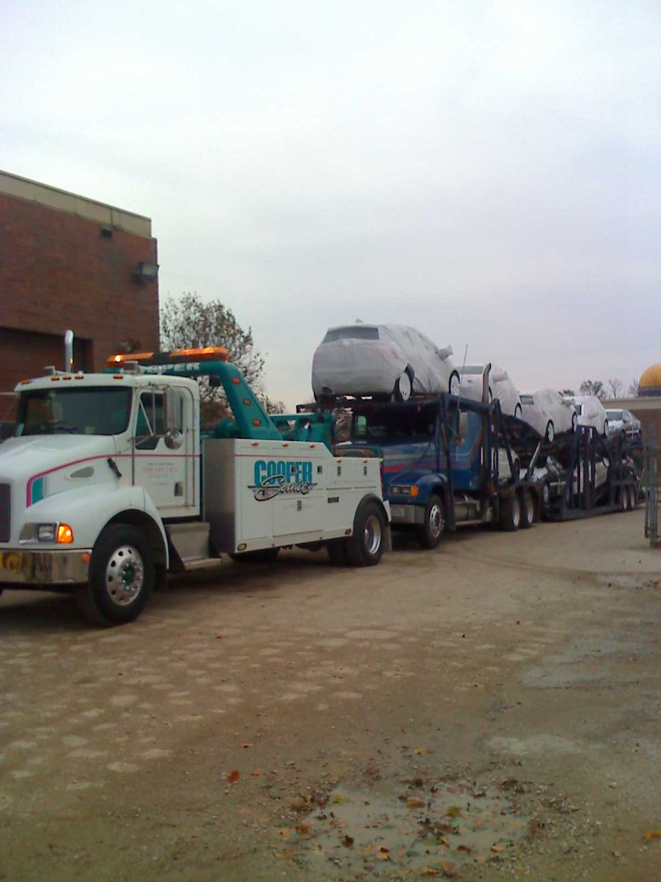 Tow truck with 'Cooper Service' on the side, hauling a car carrier full of vehicles