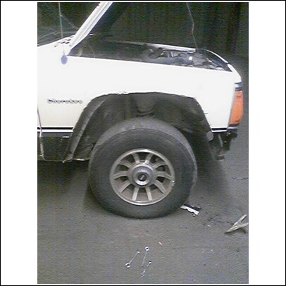 1985 Ford Bronco - A white SUV sits with its hood open, revealing the engine bay and front wheel assembly.