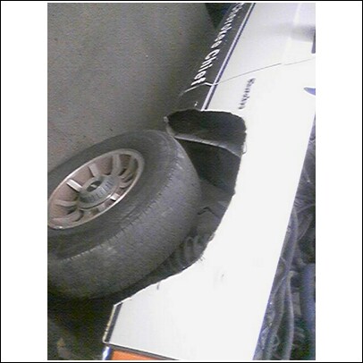 1985 Ford Bronco - The side panel and wheel well of a white 1985 Ford Bronco are visible, showing a black stripe and some damage.