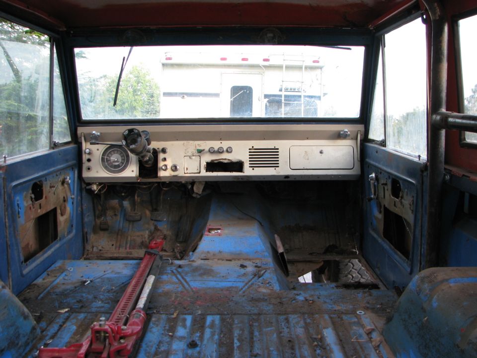 Interior of a blue 1966 Ford Bronco with a red jack on the floor, showing the dashboard and empty cabin