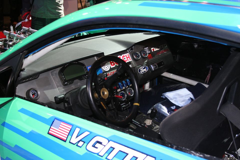 Interior of a race car with a racing steering wheel, multiple gauges, and a digital display. The dashboard has Ford and Bosch logos