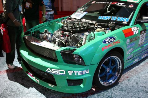 1998 Ford Crown Victoria - A green race car with its hood open, revealing the engine, and various sponsor decals on its body.