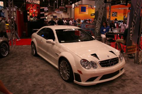 1998 Ford Crown Victoria - White Mercedes-Benz coupe with custom hood vents and wide fenders displayed at an auto show.