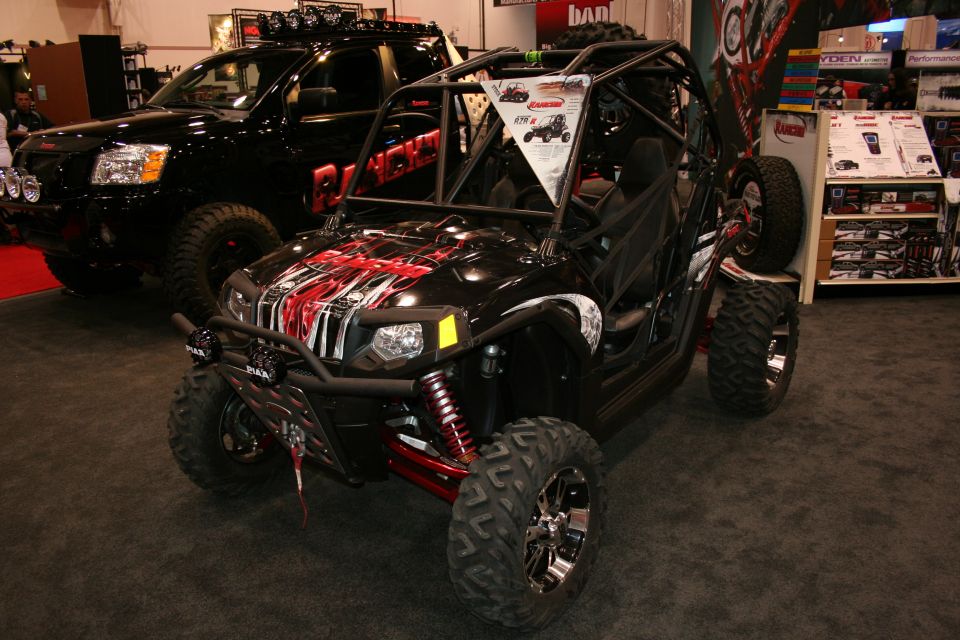 Black off-road buggy with red and white graphics, front 3/4 view. Another black truck is behind it