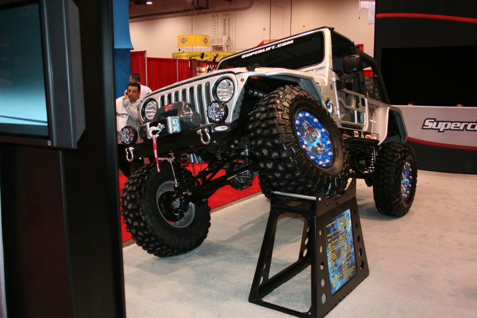 Modified Jeep Wrangler with large tires on a display stand, blue lug nuts visible
