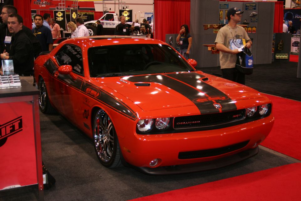 Orange Dodge Challenger with black racing stripes on display, showing 'Challenger' badge on grille
