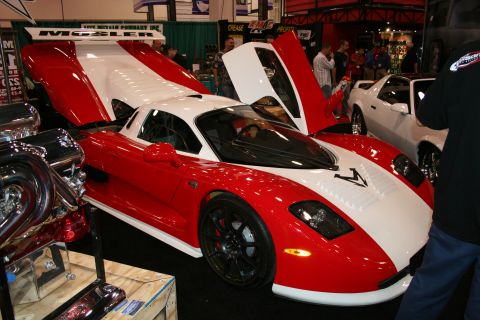 1998 Ford Crown Victoria - A red and white Mosler sports car is displayed with its butterfly doors open, alongside other vehicles and engine parts.