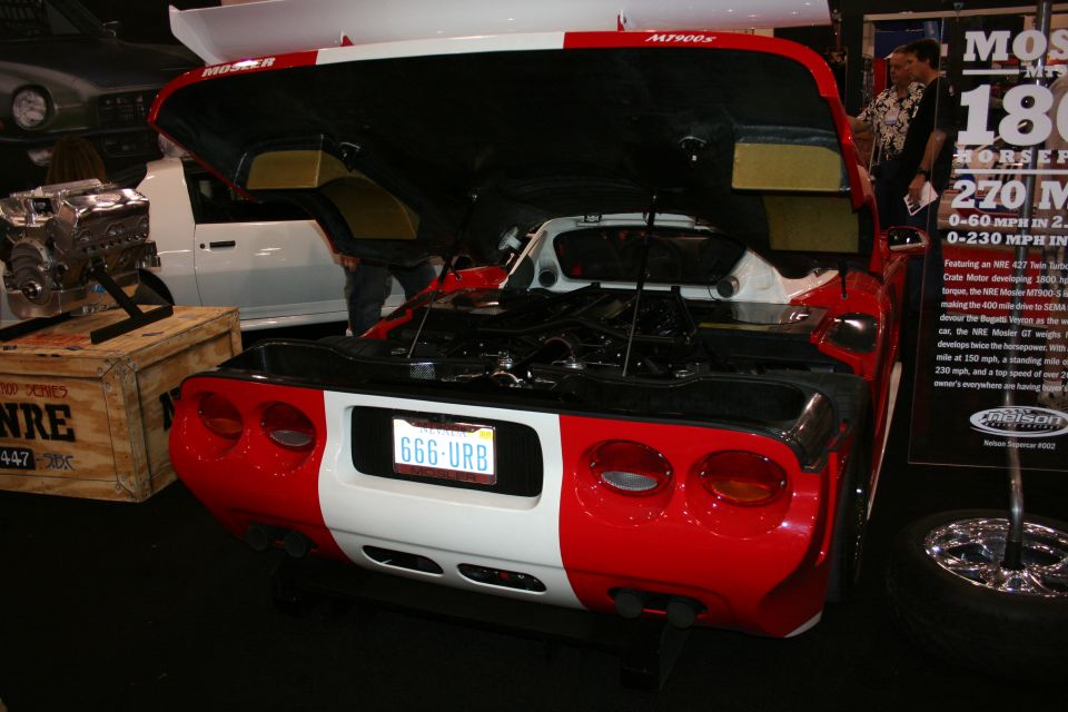 Rear view of a red and white sports car with its hood open, showing the engine bay. License plate reads 666-URB