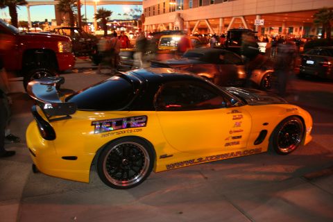 1998 Ford Crown Victoria - A yellow sports car with racing decals is parked on a street at dusk, with other vehicles and people in the background.
