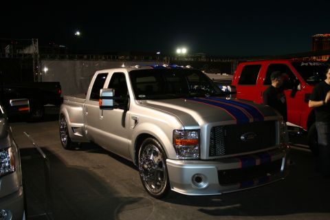 1998 Ford Crown Victoria - A customized silver Ford Super Duty truck is parked outdoors at night, with a red truck visible to its right.
