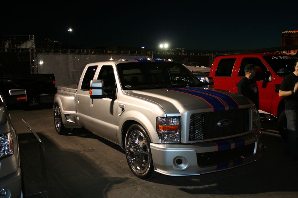 Silver Ford F-Series Super Duty truck with blue racing stripes parked next to a red truck