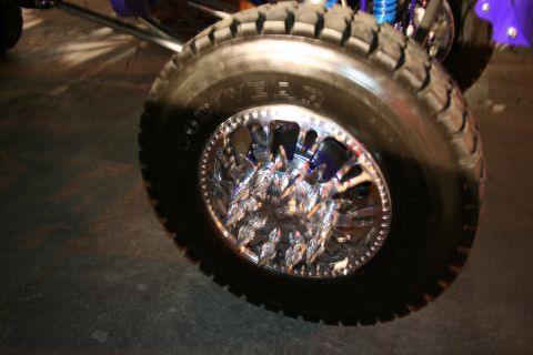 1998 Ford Crown Victoria - A heavily modified vehicle's wheel and tire assembly is shown, custom chrome rims and off-road tires.
