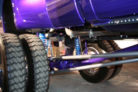 1998 Ford Crown Victoria - Close-up view of the undercarriage of a custom purple truck, highlighting its dual rear wheels and vibrant blue suspension components.
