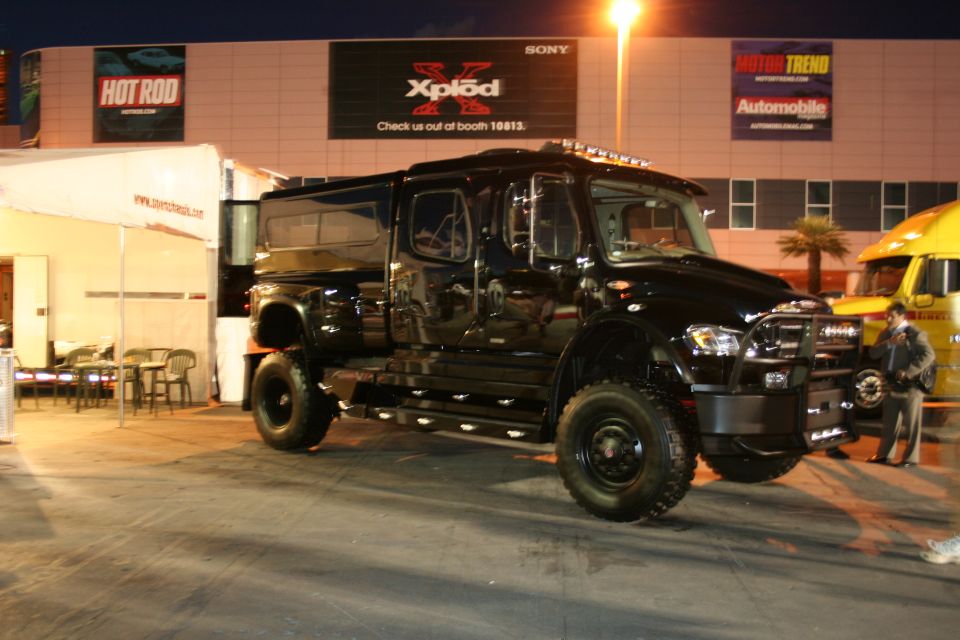 Big black custom truck with crew cab and extended bed, parked outside at night near a yellow truck