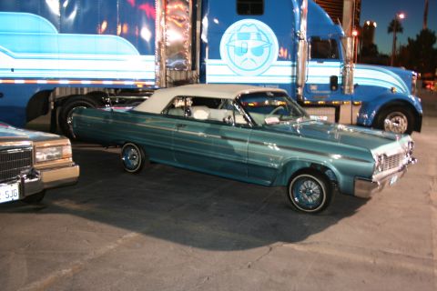 1998 Ford Crown Victoria - A classic teal convertible lowrider is parked in front of a large blue semi-truck.