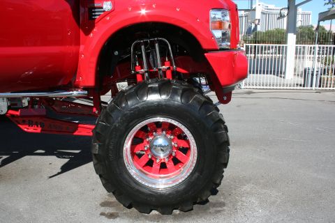 1998 Ford Crown Victoria - Close-up of a red lifted truck's front wheel and suspension system, its custom modifications.