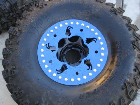 1971 Ford Bronco - A close-up view of an off-road tire a bright blue beadlock ring with stylized goat cutouts.