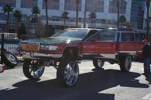 1998 Ford Crown Victoria - A heavily modified Cadillac limousine with an extended body and oversized chrome wheels is parked outdoors.