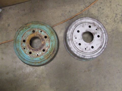 1967 Ford Bronco - Two brake drums, one showing significant rust and a blue coating, the other cleaned and painted gray.