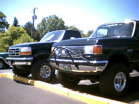 1988 Ford Bronco - Two black Ford trucks are parked next to each other on a sunny day.