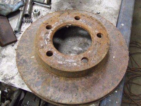 1967 Ford Bronco - A heavily rusted brake rotor is shown, with various tools scattered around it on a workbench.