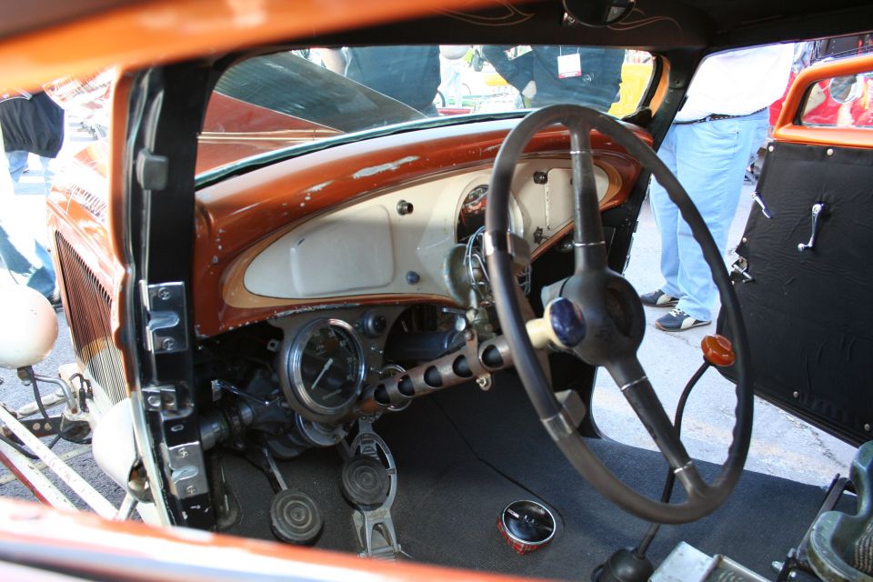 Interior view of a classic car with a wood-grain dashboard, large steering wheel, and exposed pedals