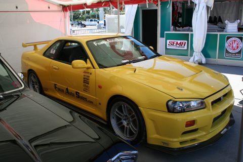 1998 Ford Crown Victoria - A yellow coupe with racing decals and a spoiler is parked next to another vehicle, with SEMA signage visible in the background.