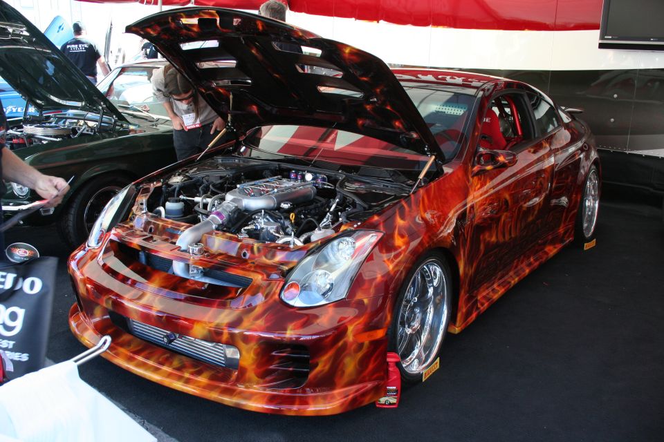 Customized coupe with flame paint, hood open showing engine, chrome rims, red racing seats