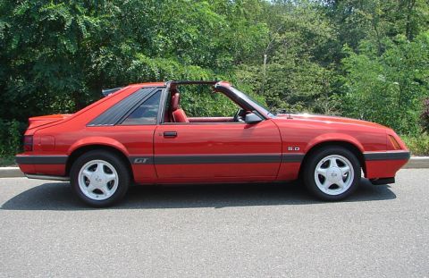1994 Ford Bronco - Side view of a red convertible sports car with GT and 5.0 badging.