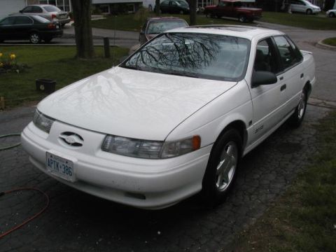 1993 Ford Taurus - A white 1993 Ford Taurus is parked in a driveway with other vehicles visible in the background.