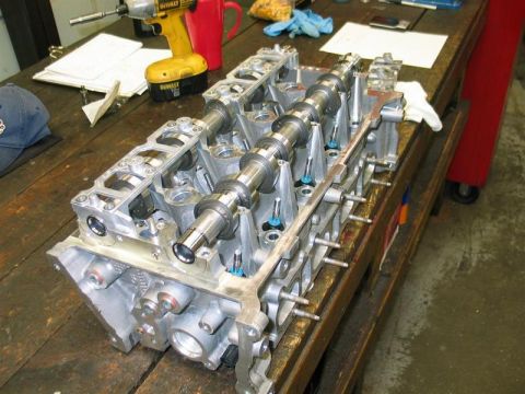2007 Ford Mustang - A disassembled engine cylinder head with camshafts is visible on a workbench, alongside tools and a mug.