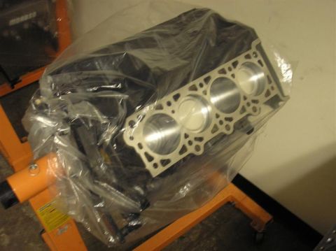 2007 Ford Mustang - Engine block and cylinder head assembly on an engine stand, wrapped in protective plastic.