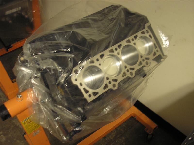 Engine block with pistons and cylinder head, covered in plastic, on an orange engine stand