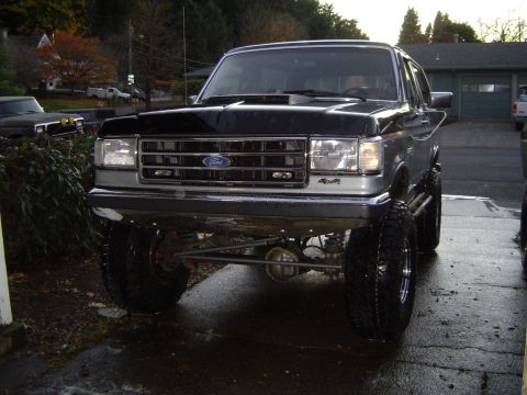 1989 Ford Bronco - This lifted Ford Bronco is parked on a wet driveway, showing off its large tires and off-road suspension.