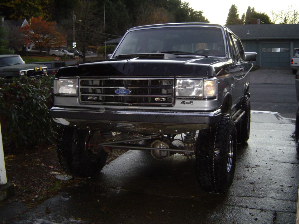Front view of a black lifted Ford 4x4 SUV with large off-road tires on wet pavement