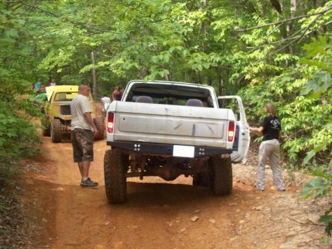 White Ford Bronco from rear, lifted, off-road tires, open driver door, on dirt road