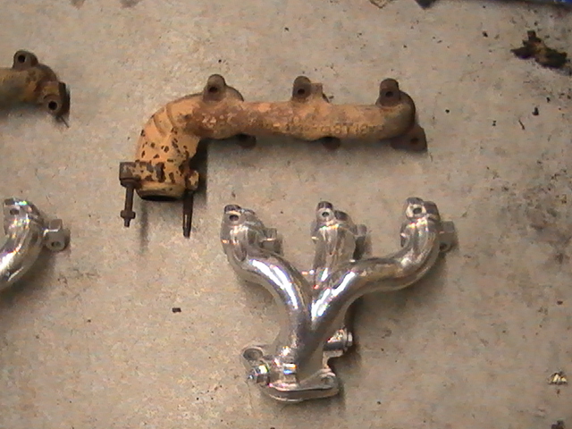 two exhaust manifolds on concrete floor, one rusty, one shiny