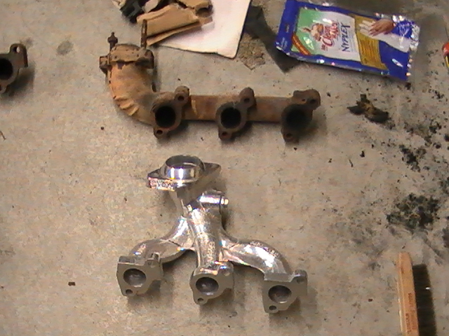 Two exhaust manifolds on a concrete floor; one is rusty and old, the other is shiny and new