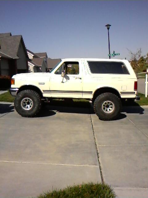 1987 Ford Bronco - A white 1987 Ford Bronco is parked on a concrete driveway under a clear blue sky.