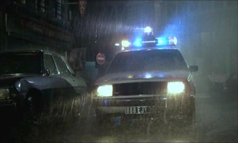 1991 Ford Crown Victoria - A police car with its emergency lights on is seen in the rain at night, with another vehicle beside it.