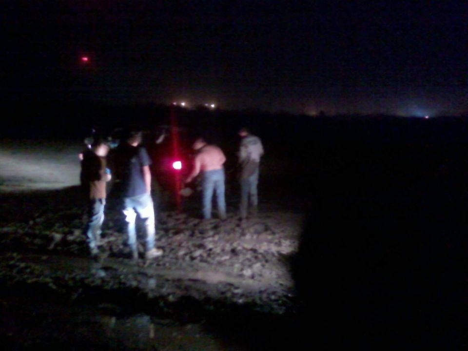 Group of people gathered at night near a red light in a muddy field