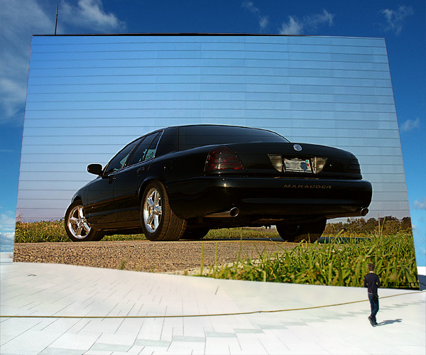 Black 2003 Mercury Marauder sedan, rear 3/4 view, parked on gravel in front of a mirrored building