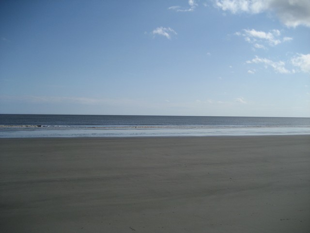Sandy beach with gentle waves under a blue sky with scattered clouds