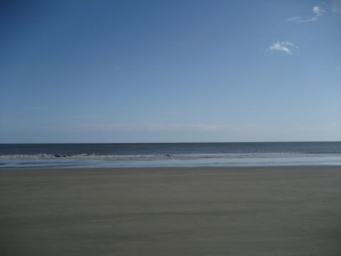 1995 Ford Bronco - A tranquil beach scene with gentle waves lapping the shore under a vast blue sky.