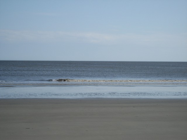 Ocean waves lap onto a sandy beach under a pale blue sky