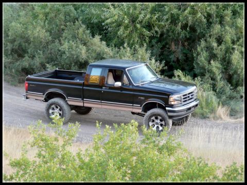 1996 Ford Bronco - Lifted black Ford F-150 pickup truck on a dirt road.