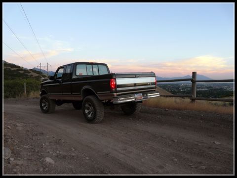 1996 Ford Bronco - A lifted black Ford F-Series truck is parked on a dirt road overlooking a valley at sunset.